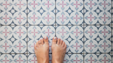 Young female bare feet with a ring on a toe on a light tile with a Turkish - Moroccan pattern. View from above.