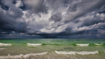 A storm with a rainbow on the Gulf of Mexico with a boat going by and the surf in the foreground.