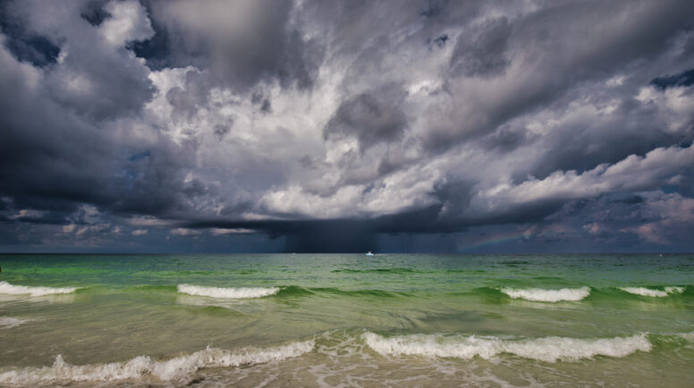 A storm with a rainbow on the Gulf of Mexico with a boat going by and the surf in the foreground.