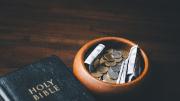 One tenth or tithe is basis on which Bible teaches us to give one tenth of first fruit to God. coins with Holy Bible. Biblical concept of Christian offering, generosity, and giving tithes in church.