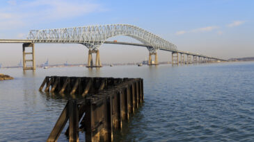 "Photo of the Francis Scott Key Bridge on a beautiful spring morning with a rusted old retaining wall in the foreground. This bridge is also known as the Outer Harbor Bridge. It is a continuous truss bridge spanning the Patapsco River, and is the third longest span of any continuous truss bridge in the world. It opened in 1977 and is named for Francis Scott Key, the author of the Star Spangled Banner."