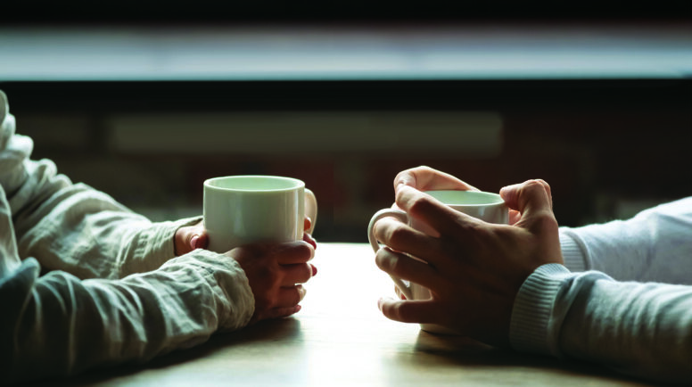 Close up woman and man sitting in cafe, holding warm cups of coffee on table, young couple spending weekend in cozy coffeehouse together, romantic date concept, visitors drinking hot beverages