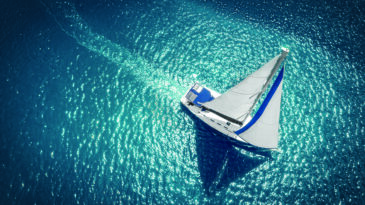 Regatta sailing ship yachts with white sails at opened sea. Aerial view of sailboat in windy condition.