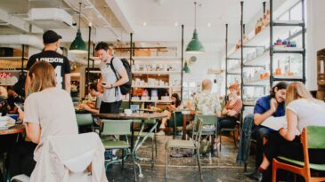 a busy coffee shop where people are talking at tables and smiling